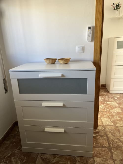 Cómoda blanca con cestas tejidas en apartamento de Matalascañas con vistas al mar, múltiples cajones y diseño moderno