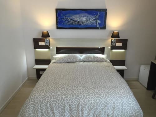 Modern single bedroom at Hotel Skyline Alcorcón with queen bed, black nightstands, lamps, and blue artwork above headboard
