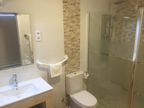 Modern bathroom in Hotel Skyline Alcorcón with white sink, toilet, walk-in shower with glass enclosure, brick tile accents,
