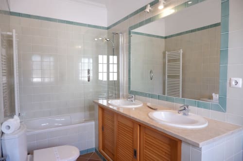 Modern bathroom in Be SilverCoast apartment with dual sinks, glass shower, and teal tile accents