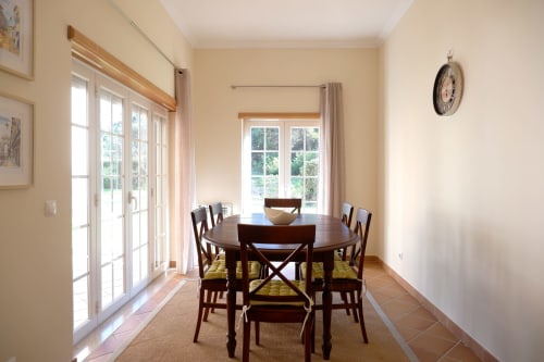 Bright dining room at Be SilverCoast with round wooden table, yellow cushioned chairs, and garden views through French doors
