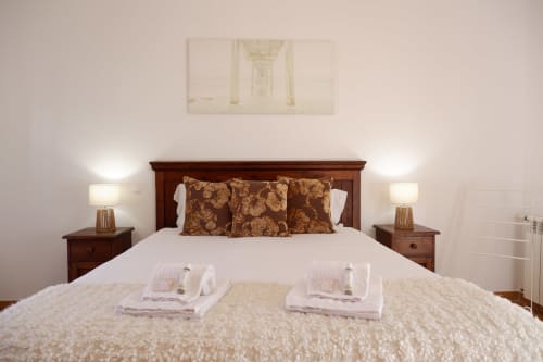Elegant bedroom at Be SilverCoast with dark wood bed, gold patterned pillows, white linens, and twin nightstands with lamps