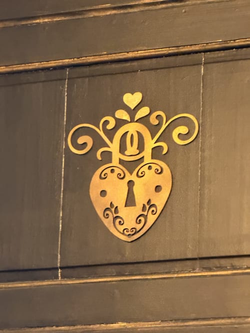 Golden ornamental heart-shaped lock with crown on dark door at La Maison Defendue, Tessy-Bocage