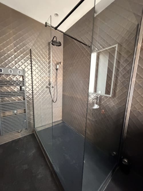 Modern walk-in shower with gray tile walls, glass enclosure, and rainfall showerhead at La Maison Defendue hotel in
