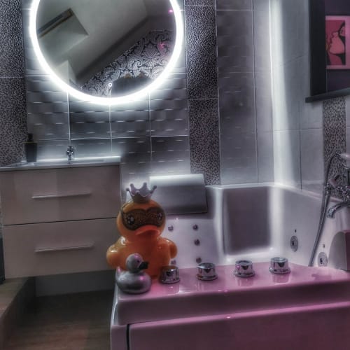 Modern bathroom at La Maison Defendue with LED-lit circular mirror, pink accent lighting, decorative duck figurine, and