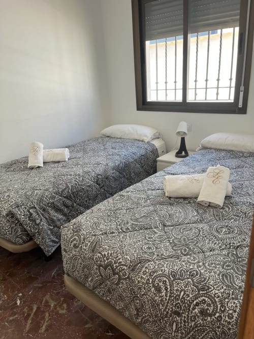 Habitación doble con colchas estampadas, toallas enrolladas y ventana con vistas al mar en Apartamentos A la Orilla del Mar, Matalascañas