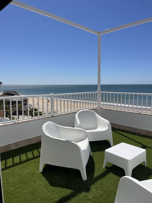 Terraza de apartamento frente al mar en Matalascañas con sillas blancas, vistas al océano y pérgola