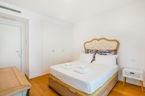 Quarto luxuoso do Atlantic Places Albufeira com cama em madeira, cabeceira creme, roupa de cama branca e guarda-roupa moderno