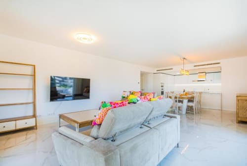 Apartamento de luxo em Albufeira com sala moderna, sofá cinzento, TV na parede e cozinha aberta com vista da cidade