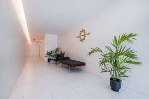 Corredor moderno no Atlantic Places Albufeira com azulejos brancos, plantas em vasos, bancos e iluminação ambiente