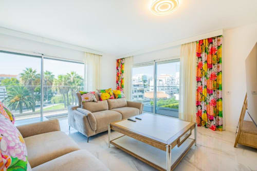 Apartamento de luxo moderno em Albufeira com sofá bege, cortinas coloridas, vista da cidade e palmeiras da varanda