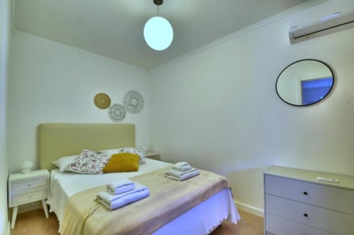 Quarto aconchegante em Atlantic Places Albufeira com cabeceira amarela, luminária pendente moderna e placas decorativas na parede