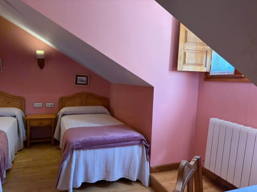 Dormitorio rosa en la buhardilla del Hotel Restaurante Casa Manolo en Adra con dos camas de madera, ropa de cama blanca, radiador y claraboya