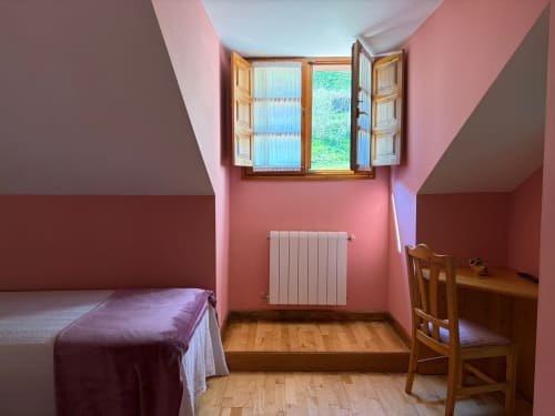 Habitación rosa en Hotel Casa Manolo en Adra con cama de madera, escritorio, radiador y ventana abierta con vistas a vegetación