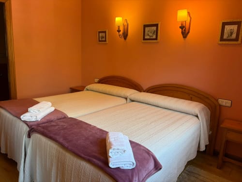 Luminosa habitación naranja en el hotel Casa Manolo de Adra con dos camas individuales, cabeceros de madera, sábanas blancas y apliques de pared