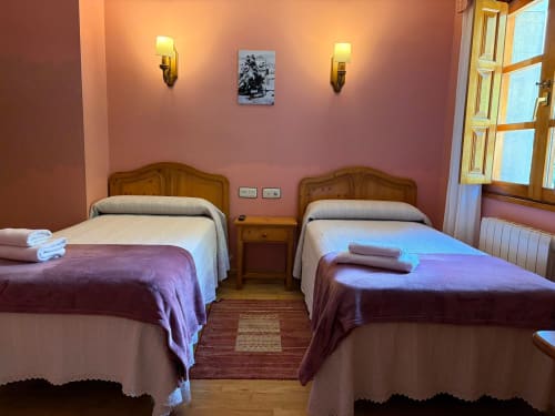 Habitación doble en Hotel Restaurante Casa Manolo de Adra con camas de madera, ropa de cama morada y paredes rosa cálido