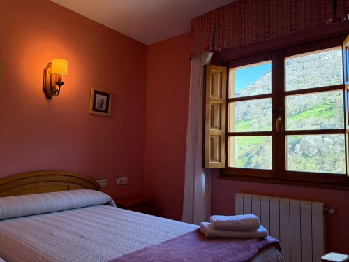 Cálida habitación roja con cama doble, ventanas con vistas a la montaña, lámpara de pared y radiador en Hotel Restaurante Casa Manolo