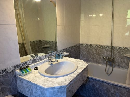 Baño moderno del hotel Casa Manolo con vanitory de mármol, lavamanos redondo, cenefa decorativa y bañera con mampara de cristal