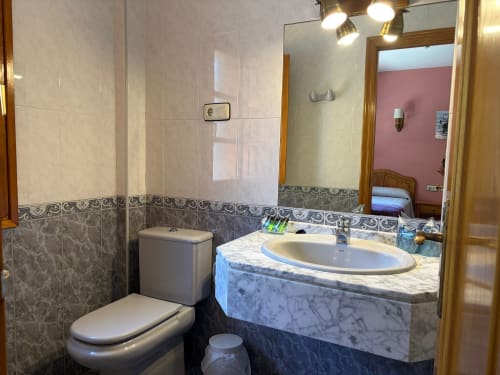 Baño moderno del Hotel Casa Manolo en Adra con lavamanos de mármol, inodoro, ducha y detalles decorativos de azulejos