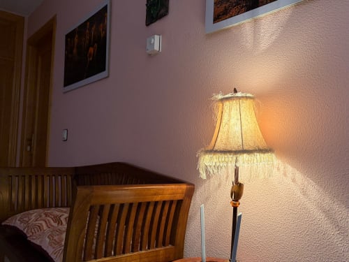 Rincón de habitación de hotel iluminado cálidamente con silla de madera, lámpara decorativa de pantalla con flecos y paredes texturadas rosa en Casa Manolo