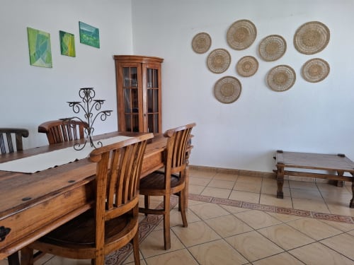 Dining area in Villa 9 at Villas del Mar with wooden table, chairs, woven baskets, and green artwork on white walls