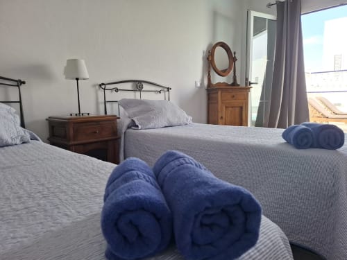 Cozy bedroom at Villas del Mar with twin beds, blue rolled towels, wooden nightstand, and mountain views through balcony