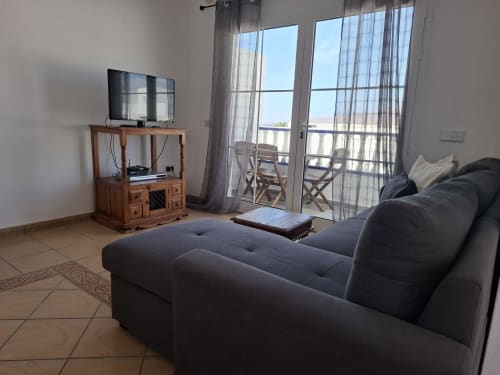 Modern villa living room with dark sofa, flat-screen TV, wooden entertainment unit, and terrace view at Villas del Mar Puerto