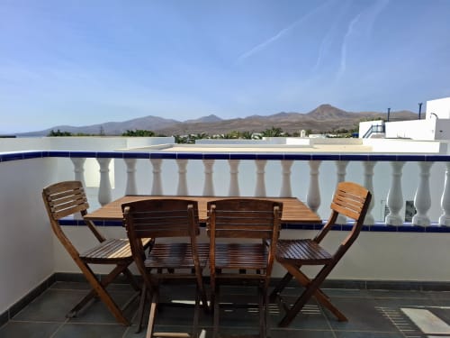 Wooden dining table and chairs on a terrace at Villa 9 in Puerto Calero, with mountain views and pool railing