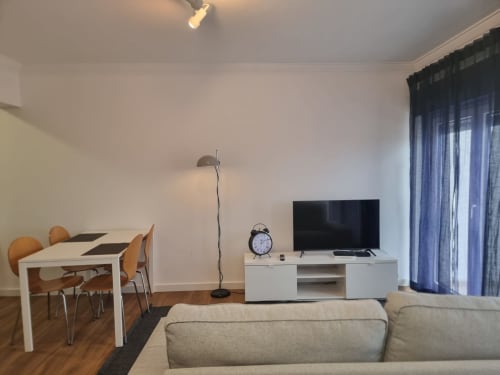 Modern apartment living room at Ericeira Property with dining table, sofa, TV, and floor lamp