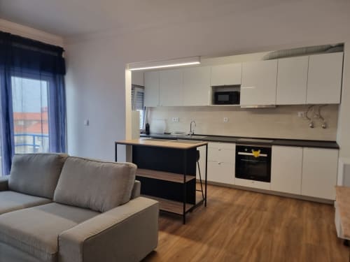 Modern open-plan kitchen and living area at Ericeira Property with cream cabinetry, island counter, and gray sofa