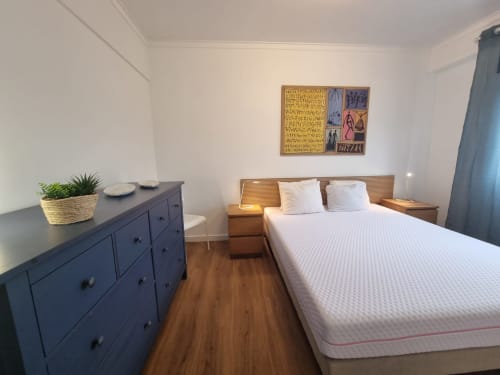 Modern bedroom at Ericeira Property with queen bed, blue dresser, wooden nightstands, and white walls