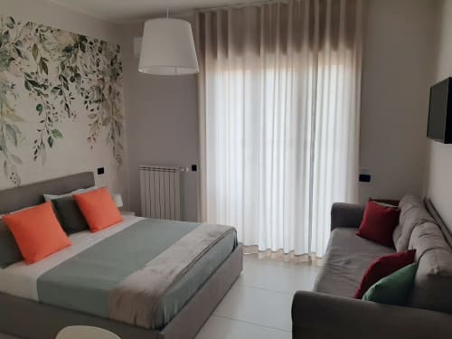 Camera moderna presso My Comfort Suite Naples con letto queen, biancheria grigia, cuscini arancioni, TV a schermo piatto e balcone con