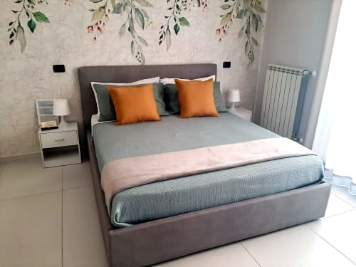 Camera moderna presso My Comfort Suite Naples con letto grigio, cuscini arancioni, carta da parati botanica e vista sulla città