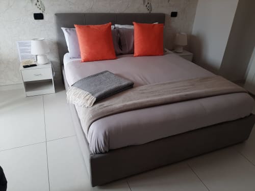 Camera moderna presso My Comfort Suite Naples con letto queen, testata grigia, cuscini arancioni, comodino bianco e vista mare
