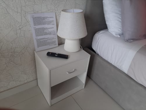 Comodino bianco con lampada, telecomando e documenti nella camera di My Comfort Suite Naples