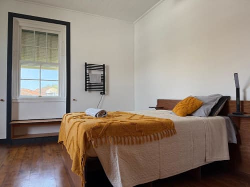 Bright bedroom at Golden Mermaid Villa with wooden bed, mustard blanket, window with landmark views, and hardwood floors