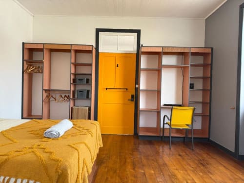 Quarto luminoso na Villa Golden Mermaid com cama amarela, porta laranja, prateleiras de madeira e piso de madeira