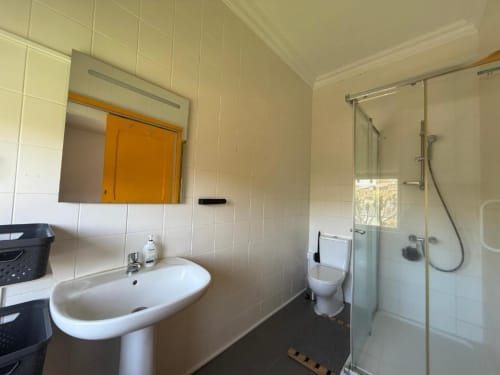 Banheiro moderno da Villa Golden Mermaid com pia coluna, vaso sanitário, box de chuveiro e espelho com moldura amarela