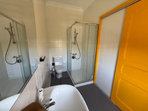 Banheiro claro na Villa Golden Mermaid com banheira, duchas duplas, vaso sanitário e porta amarela característica