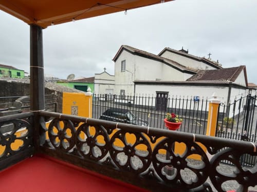 Vista do terraço da Villa Golden Mermaid com balaustrada ornamentada, vista para capela branca e portões amarelos em Portugal
