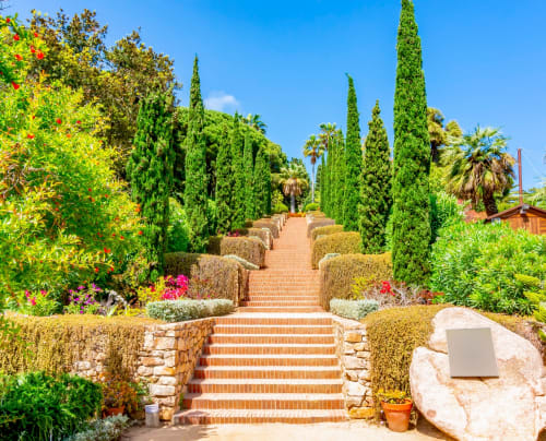 Escaleras del jardín del hotel Tr3sor con cipreses, flores coloridas y paisaje mediterráneo