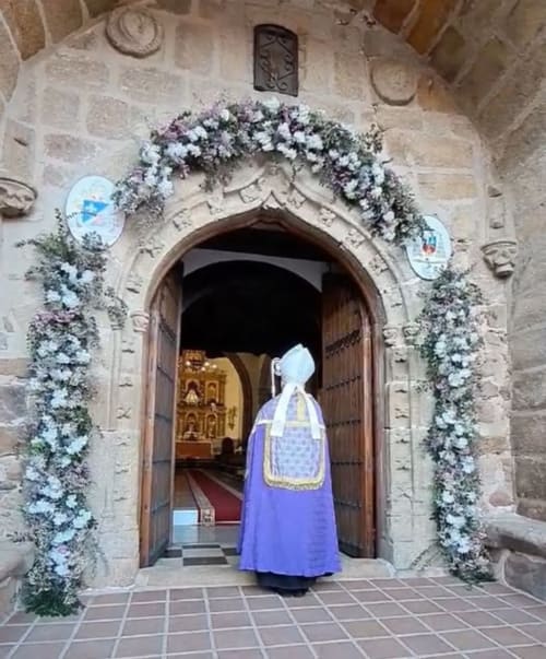 Religiöse Person in blauem Gewand betritt verzierte Steintor in El Escudo De Calatrava, Toledo Spanien