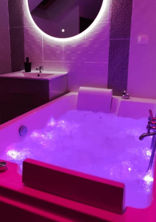 Salle de bains moderne à La Maison Defendue avec éclairage néon violet, miroir circulaire illuminé et baignoire remplie