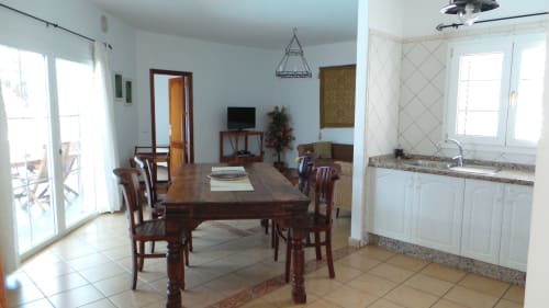 Open-plan dining and kitchen area in Villa 2 at Villas del Mar, Puerto Calero, with wooden table, white cabinetry, and bright