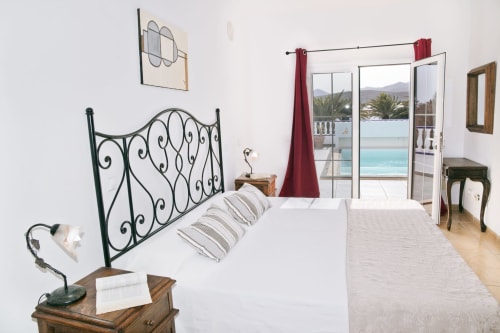 Dormitorio luminoso en villa con cama de hierro ornamental, vistas al océano y montañas por puertas acristaladas, terraza privada en Puerto Calero