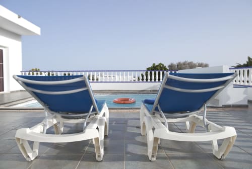 Two blue and white lounge chairs facing private pool at Puerto Calero villa with white railing and clear sky