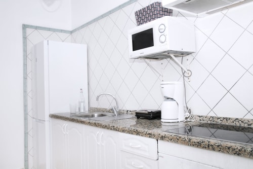 Modern white kitchen with granite countertop, microwave, appliances, and diagonal tile backsplash in Villa 3 at Villas del