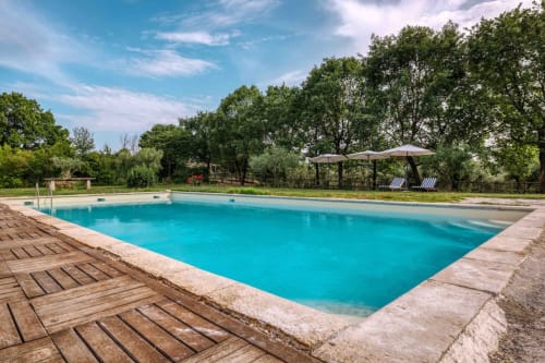 Piscina turchese a Donkeys & Roses a Viterbo con solarium in legno, ombrelloni e alberi verdeggianti