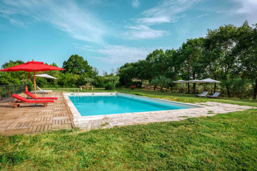 Piscina turchese con lettini rossi e ombrellone presso Donkeys & Roses vicino Viterbo, circondata da giardini verdeggianti