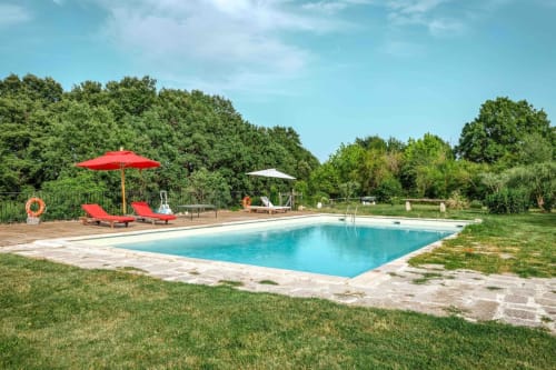 Piscina azzurra presso Donkeys & Roses a Viterbo con lettini rossi, ombrelloni e giardini verdi.